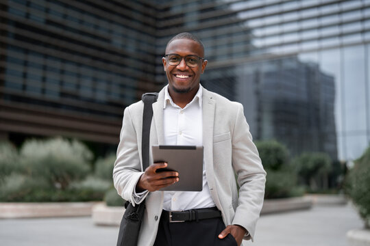 Portrait of african american businessman, entrepreneur, using tablet, checking analytics, outdoor near office building. Black business man smiling, reviewing project details, managing accounts.