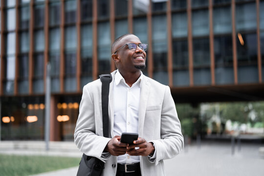 Entrepreneur, black businessman, using smartphone, calling, outdoor near office building. African american business man smiling, staying connected with technology, building strong client partnerships.
