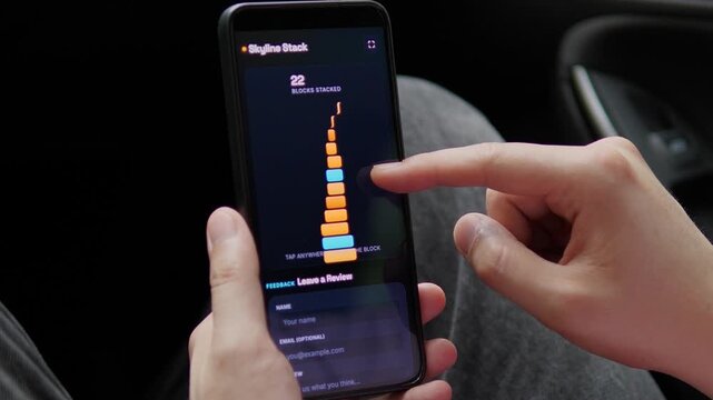 Player builds a glowing block tower on a smartphone until it collapses at a new high score, capturing casual mobile gaming, focus, timing and digital entertainment culture.
