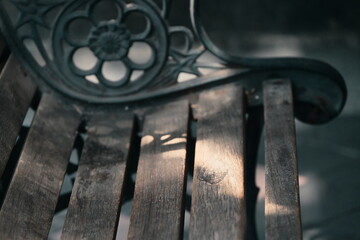 Fototapeta premium Ornate cast iron armrest and wood backrest slats show grain cracks, uneven color, sun-worn peeling, damp surface, afternoon light, Zhongzheng, Taipei.