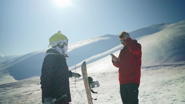Two friends high-five on a snowy mountain while enjoying a winter snowboarding trip. A man and a woman in winter gear share a moment of joy on the ski slope.