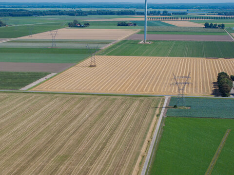 Aerial view of agricultural fields with power lines, a wind turbine, and a rural road in the Netherlands.