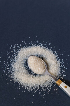 Top view of spoonful raw cane sugar crystals surrounded by scattered granules on dark background with copy space
