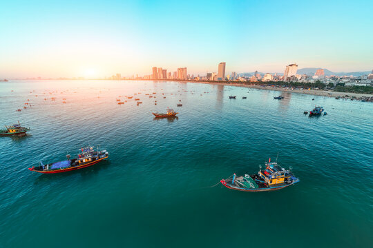A long-tail boat sails across Chao Phraya River as the sun sets behind Wat Arun, the iconic Temple of Dawn in Bangkok, Thailand. The sky shows warm colors.