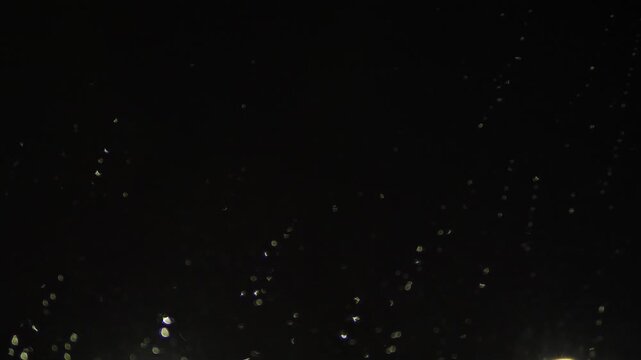 Small raindrops slowly trickle down a dark window in the silence of the night. Sparse bottom lighting illuminates the water droplets, creating an atmospheric minimalist background