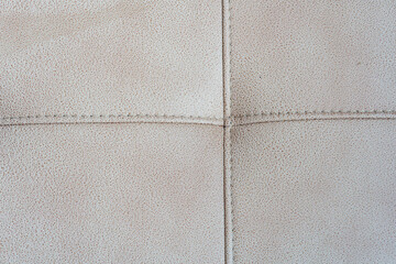 Fototapeta premium Close-up of a beige tufted leather upholstery texture with stitched crossed seams