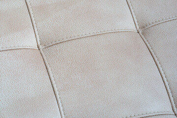 Obraz premium Close-up of a beige tufted leather upholstery texture with stitched crossed seams
