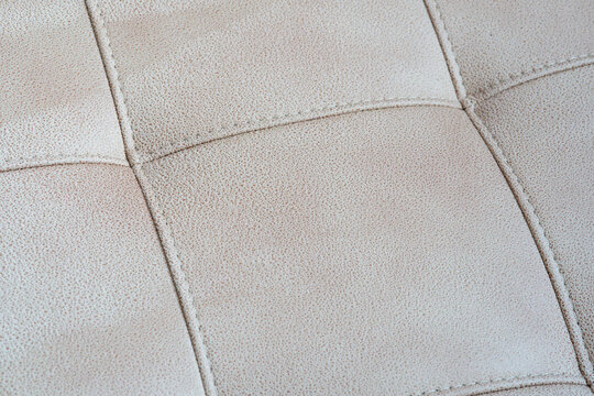 Close-up of a beige tufted leather upholstery texture with stitched crossed seams
