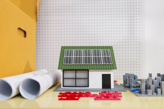 Miniature house model with solar panels on the roof, next to rolled blueprints and building materials, green home energy and construction planning
