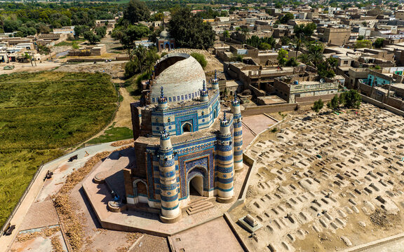 Aerial view of the historic Tomb of Bibi Jawindi featuring its iconic blue-tiled facade, partially collapsed dome, and surrounding ancient cemetery in Uch Sharif, Punjab, Pakistan.