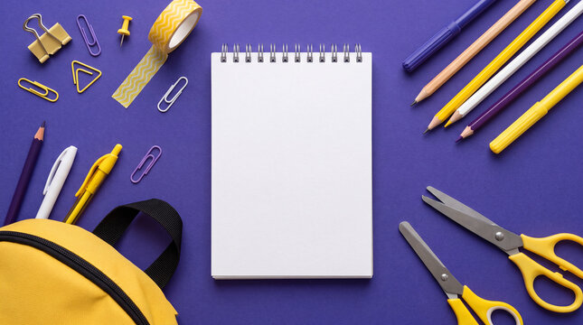 Flat lay of blank notepad with yellow and purple school supplies, pencils, scissors, clips, and backpack on purple background. Space for text.