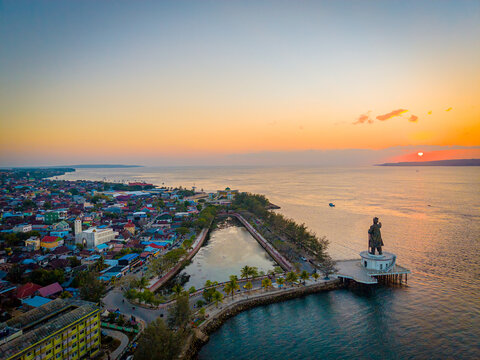Aerial view of the Oputa Yi Koo statue on a platform over the sea at sunset, with the coastal city of Bau-bau and its urban rooftops in Bau-bau, South East Sulawesi, Indonesia.