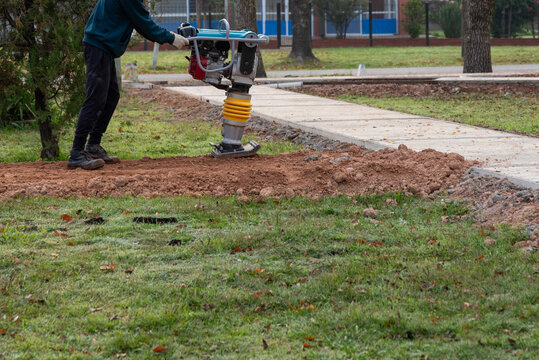 Construction worker operating jumping jack tamping rammer for soil compaction in public works