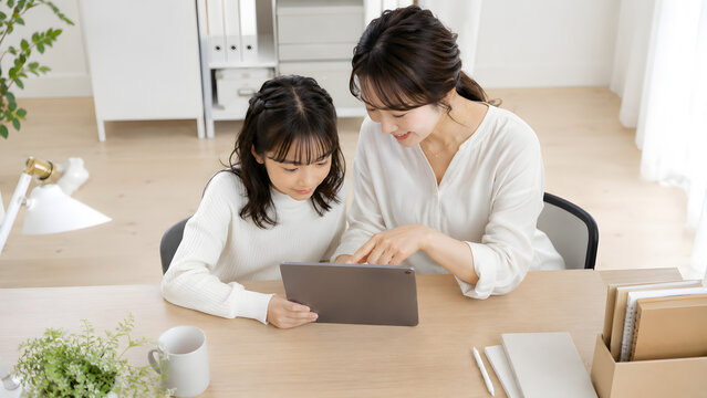 明るいリビングのデスクでタブレットの画面を一緒に見ながら微笑む母親と娘
