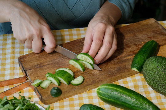 Hands slicing cucumber for salad on wooden board. Food prep. 