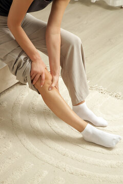 Woman Holding Painful Knee While Sitting on Bed, Knee Pain and Joint Discomfort Concept
