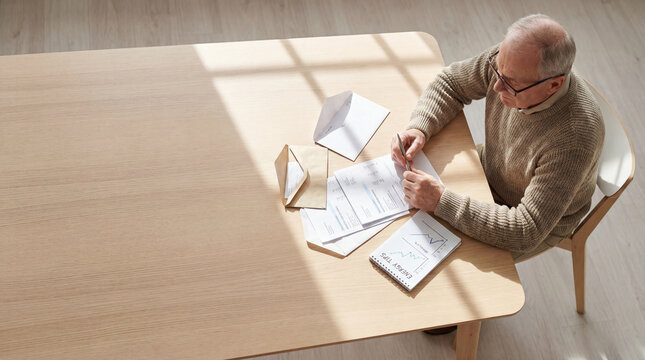 Senior man reviewing household energy bills rising cost charts at table, authentic active aging concept showing independence confidence value value value value value value value value