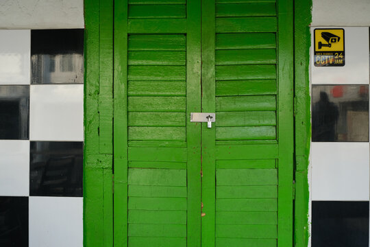 Vintage green wooden shutter door with padlock, flanked by black and white tiled walls and a CCTV surveillance sign