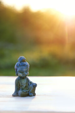 beautiful miniature stone Buddha figurine outdoor, abstract sunny natural background. landscape with cute little Buddhist monk figurine. symbol of religion, meditation, harmony, yoga. soft focus