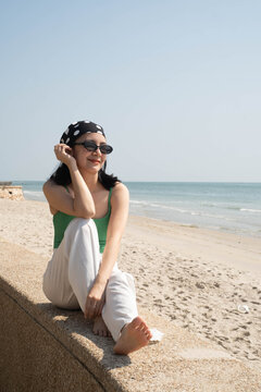 Young woman relaxing barefoot by a sandy beach, enjoying a peaceful ocean view on a sunny day. Summer vacation, coastal lifestyle, wellness, seaside travel, freedom, leisure, and copy space.
