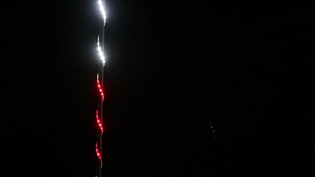 Vertical string of glowing white and red LED lights against a pitch black background.