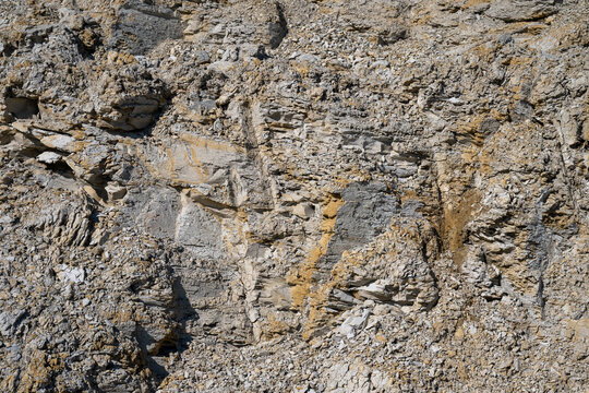 a rugged, weathered rock face featuring jagged grey and brown stones with coarse, natural textures.
