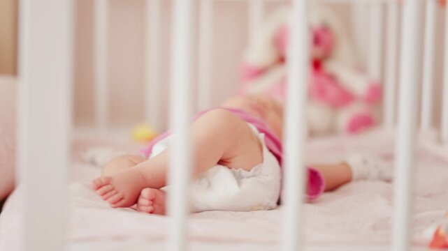 Cute baby resting inside white wooden crib with soft plush toy in background.