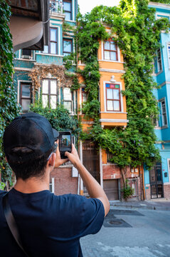 Istanbul, turkey, august 2, 2025 man holding smartphone, photographing vibrant, ivy covered historical houses in balat, istanbul, experiencing culture and travel