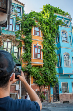 Istanbul, turkey, august 2, 2025 man documenting vibrant historic houses covered with green climbing plants in balat district, istanbul, turkey. Urban travel concept