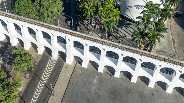 Aerial view of the historic Arcos da Lapa aqueduct featuring white arches, tram tracks on top, and surrounding palm trees in Rio de Janeiro, State of Rio de Janeiro, Brazil.