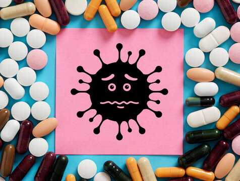 Sad Virus Cartoon Surrounded by Medical Pills and Capsules