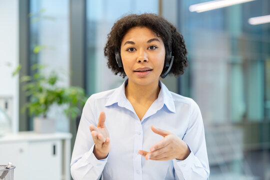 Close-up portrait of a young African American woman in a headset talking on a video call to the camera, gesturing with her hands