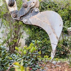 Heavy excavator ripper tooth clearing dense shrubs during residential garden landscaping work © Rawf8