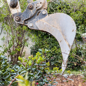 Heavy excavator ripper tooth clearing dense shrubs during residential garden landscaping work