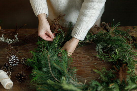 Making christmas rustic wreath. Female hands arranging fir branches to craft Christmas wreath on wooden table. Cozy DIY xmas workshop, natural eco friendly holiday home decoration.