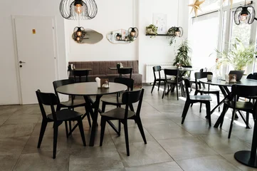 Fotobehang Horeca Bright contemporary cafe interior with stylish furniture, large windows, and decorative lighting. Cozy hospitality space prepared for guests in a modern coffee shop  © Ekaterina