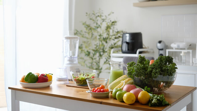 Fresh fruits and vegetables arranged on a kitchen table with salad, green juice, and blender for a healthy lifestyle concept.