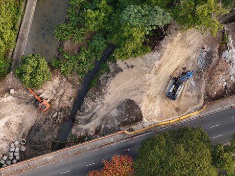 Aerial view of construction site with an excavator and drilling rig near a stream and road in Santo Domingo, Distrito Nacional, Dominican Republic.