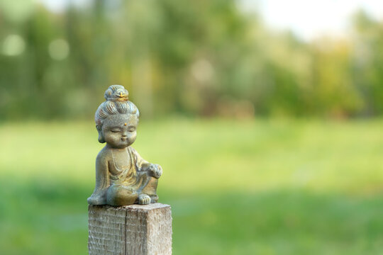 beautiful miniature stone Buddha figurine outdoor, abstract natural background. landscape with cute little Buddhist monk figurine. symbol of religion, meditation, harmony, yoga. copy space. soft focus