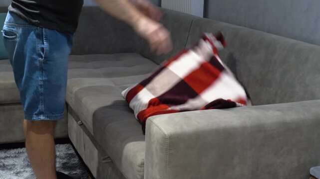 A young man is folding a blanket from the living room sofa. Folding the blanket by hand from the living room sofa