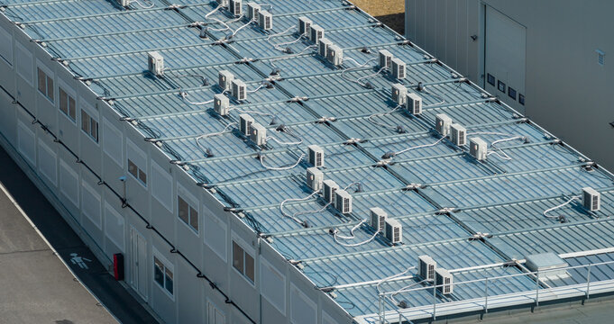Aerial view of a modular industrial building featuring numerous rooftop HVAC systems and air conditioning units at a modern technology campus in Crolles, Auvergne-Rhone-Alpes, France.