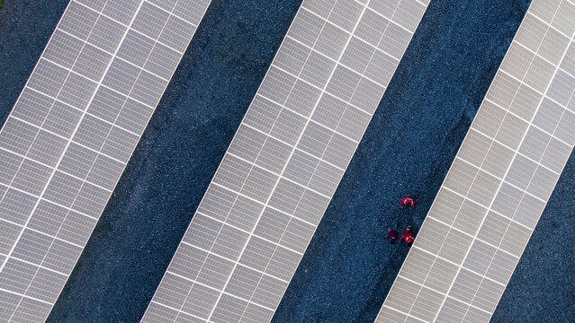 Aerial view of solar panels at a photovoltaic power plant with workers in red safety gear walking along gravel paths in Itaguai, Rio de Janeiro, Brazil.