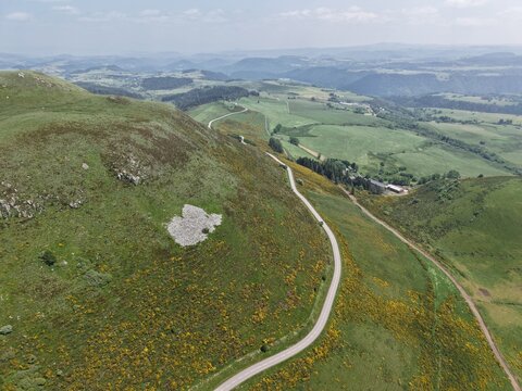 Aerial view of Col de la Croix-Morand winding through the lush green volcanic hills and meadows of the Auvergne region in Chambon-sur-Lac, Auvergne-Rhone-Alpes, France.