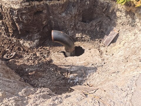 Large black metal pipe elbow exposed in a deep excavated pit during underground utility infrastructure repair.