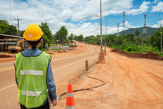 Civil engineer wearing hardhat and safety vest inspecting road construction site.