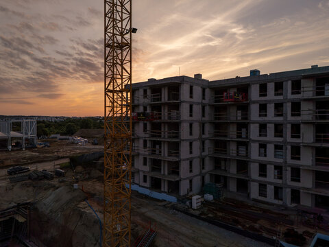 Aerial view of a construction site featuring a tall yellow crane and a multi-story building under development during a golden sunset in Gdansk, Poland.