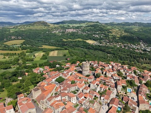 Aerial view of the historic village of Montpeyroux with its medieval tower, stone houses with terracotta roofs, and lush green rolling hills in Montpeyroux, Auvergne-Rhone-Alpes, France.