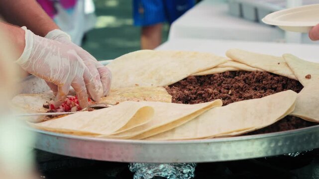 Street vendor preparing a Turkish lavash wrap with seasoned minced meat, fresh tomatoes, herbs and vegetables. Traditional street food being assembled by hand. High quality 4k footage