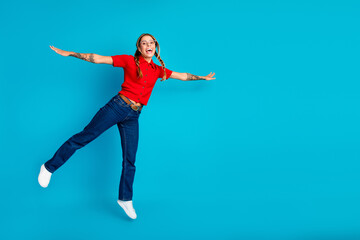 Fototapeta premium Adorable young woman jumping with joy in a red polo shirt against a blue background for lifestyle fashion and advertising