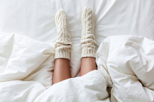 Cozy woman in knitted wool socks relaxing in bed for warm winter morning comfort